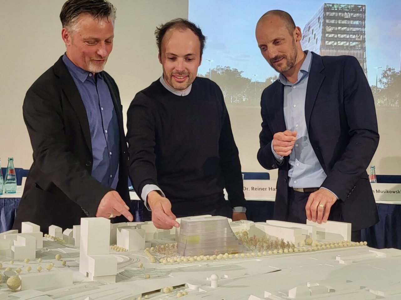 Landschaftsarchitekt Tobias Micke und die Architekten Christoph Richter und Jan Musikowski stehen hinter einem Tisch. Auf dem Tisch ist das Entwurf des Zukunftszentrums in einer 3D-Modell des Areals des Riebeckplatzes