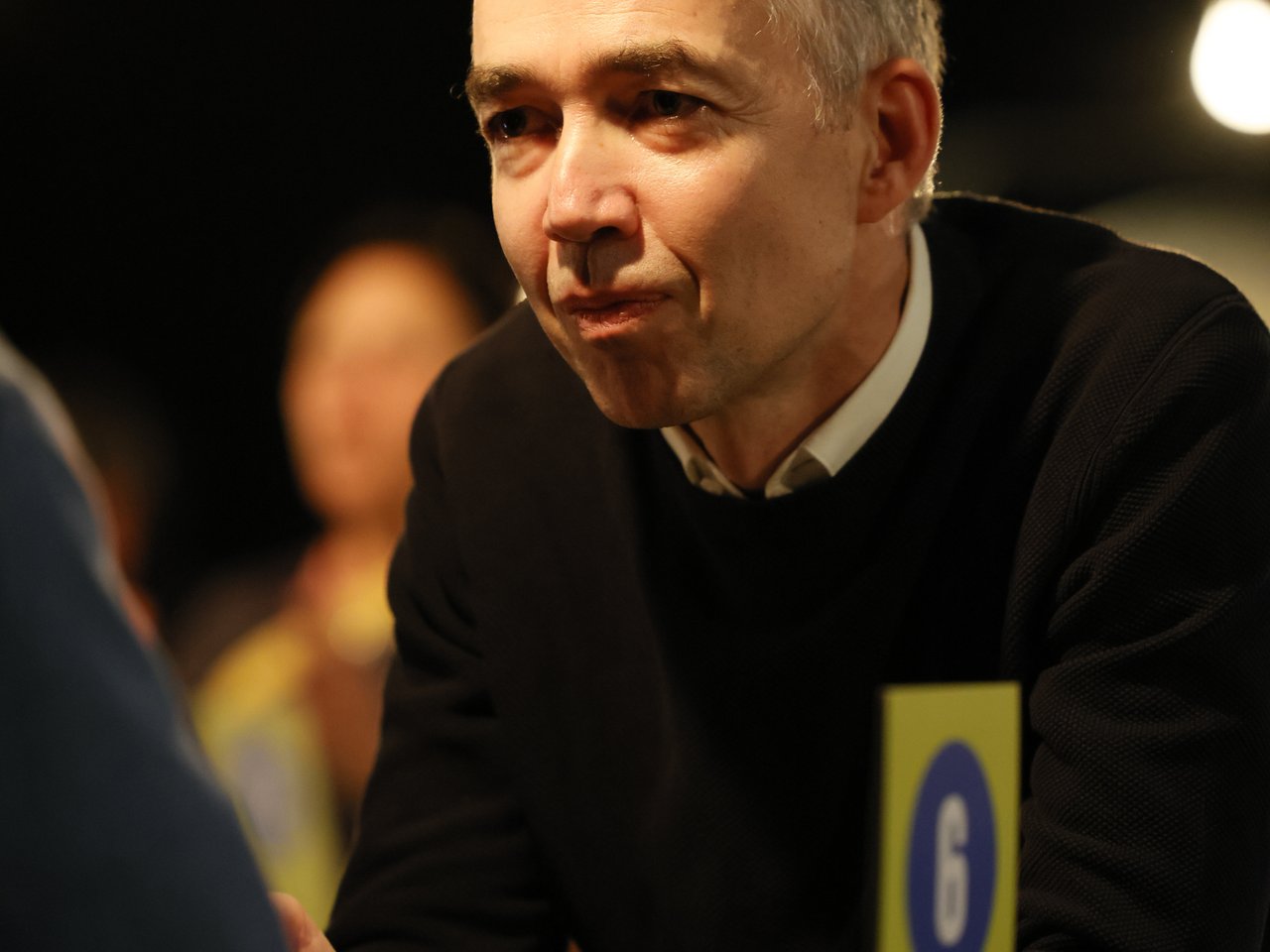 Holger Lemme, kaufmännischer Geschäftsführer des Zukunftszentrums, sitzt beim Markt für nützliches Wissen und Nicht-Wissen im neuen theater in Halle (Saale) an Tisch Nummer 6. Er trägt einen schwarzen Pullover über einem weißen Hemd und hört seinem Gegenüber aufmerksam zu. Auf dem Tisch stehen zwei Wassergläser. Im Hintergrund sind weitere Veranstaltungsgäste zu sehen.